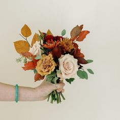 a person holding a bouquet of flowers in their hand with leaves on the top and bottom