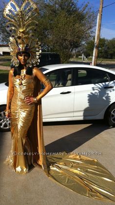 a woman in a gold dress standing next to a white car wearing a golden mask