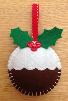 a felt ornament hanging on a wooden surface with holly and red ribbon attached to it