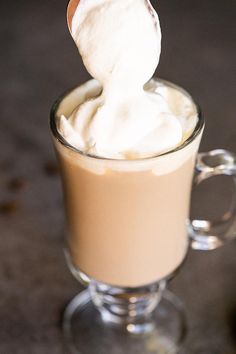 a spoon with whipped cream on it in a glass cup next to a coffee mug