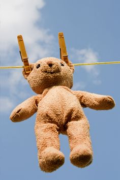 a brown teddy bear hanging from a clothes line with two pegs attached to it