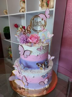 a three tiered cake with pink and purple butterflies on the top is sitting on a table