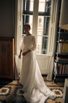 a woman standing in front of a window wearing a white dress