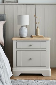 a white nightstand with two drawers and a lamp on it in a bedroom next to a bed