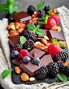 assorted chocolates, nuts, and berries on a black platter with mint leaves