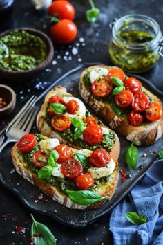 two pieces of bread topped with tomatoes and pesto on top of a black plate