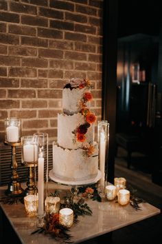 a wedding cake with flowers and candles on a table in front of a brick wall