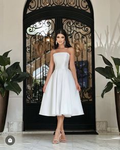 a woman standing in front of a door wearing a white dress