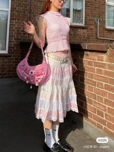 a woman is standing in front of a brick building holding a pink purse and looking at the camera