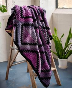 a purple and black blanket sitting on top of a wooden chair next to a potted plant