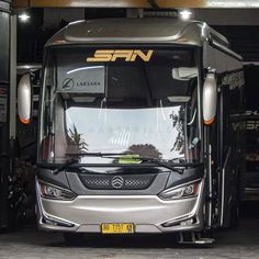 a silver bus parked in a garage next to other buses and trucks with the word span written on it