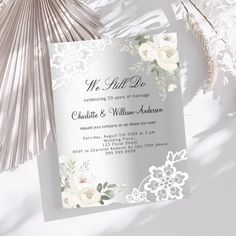 an elegant wedding card with white flowers and greenery on the front, next to a fan