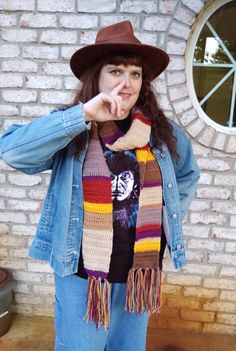 a woman wearing a hat and scarf standing in front of a brick wall with her finger on her lips