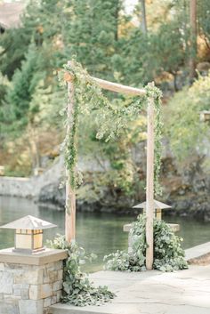 an outdoor ceremony setup with greenery and lanterns on the side of a river bank