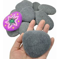 a hand holding a rock with a painted flower on it next to some rocks that have been placed together