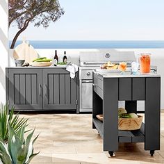 an outdoor kitchen with grill, sink and table on the patio overlooking the ocean in front of it