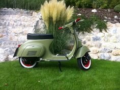 a scooter parked in the grass next to a stone wall and some plants