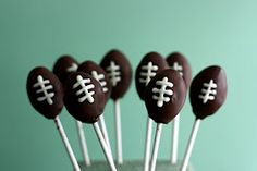 chocolate football cake pops with white frosting on green tableclothed surface, ready to be eaten