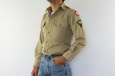 "Vintage US Army shirt  Made in USA 1940/50s Military shirt in khaki cotton twill. Long sleeves with buttons. 6 buttons front Shoulder patches Buttoned patch pockets with flaps. Shoulder tabs. Sideseam hem gussets. Contract stamp still visible but unreadable In very good condition. Some signs of wear. To note: (photos) Small stains. Small pulled threads on collar (due to grade pins). Small holes on sleeves. 100% cotton twill. Without size and composition label. Estimated size: S/M The model usually wears a size M and measures 175cm - 68.8\". Measurements taken flat: Shoulders: 39cm - 15,3\" Chest: 50cm - 19,6\" Bottom: 51cm - 20\" Length: 73cm - 28.7\" Sleeves: Length: 60cm - 23,6\" Width: 19cm - 7,4\" Please note that our items are vintage and may have slight imperfections. For more detai Retro Khaki Button-up Shirt, Retro Khaki Cotton Shirt, Vintage Khaki Tops With Snap Buttons, Vintage Khaki Button-up Shirt, Vintage Khaki Shirt With Button Closure, Retro Cotton Shirt With Buttons, Natural Leather Bag, Army Shirt, Vintage Leather Backpack