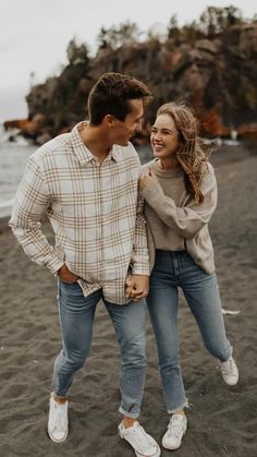 a man and woman standing on top of a sandy beach next to the ocean smiling at each other