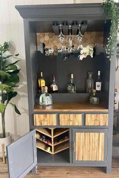 an open cabinet with liquor bottles and glasses on the top, next to a potted plant