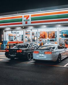 two cars are parked in front of a gas station with the lights on at night