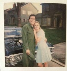 a man and woman standing next to each other in front of a car on the street