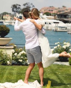 a man and woman standing on top of a lush green field next to a body of water