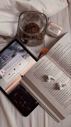 an open book sitting on top of a bed next to headphones and earbuds