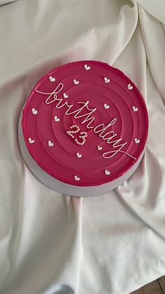 a pink cake with hearts on it sitting on a white tablecloth covered bedding