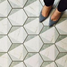 a woman's feet in grey shoes standing on a tiled floor with hexagonal tiles