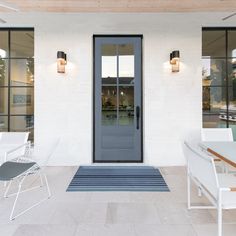 the front door of a white building with two chairs and a rug on the floor