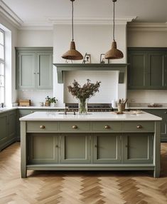 a kitchen with green cabinets and white counter tops, an island in the middle is surrounded by wood flooring