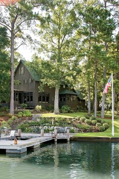 a dock sits in front of a large house on the water with chairs and an american flag flying above it