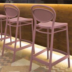 three pink stools sitting in front of a wooden wall with an illuminated bar behind it