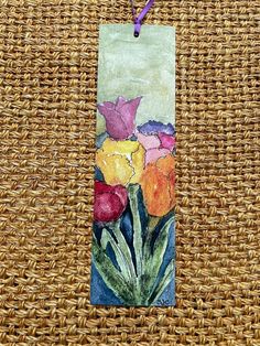 a tag with flowers painted on it sitting on a wicker tablecloth covered surface