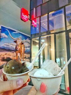 a person holding up an ice cream sundae in front of a building with a cow painting on it