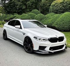 a white car parked on the side of a road next to some bushes and trees