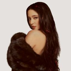 a woman with long dark hair wearing a fur coat and posing for the camera in front of a white background