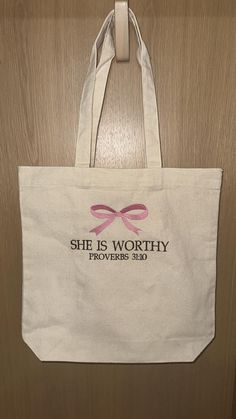 she is worthy tote bag hanging up on the door with pink ribbon around it