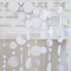 some white paper circles hanging from the ceiling in front of a window with curtains on it