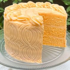 a piece of cake with white frosting on a glass plate next to a green bush