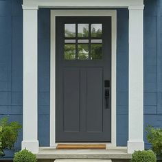 a gray front door on a blue house with white trim and columns, flanked by two potted plants