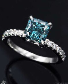 a blue diamond ring with white diamonds on the sides and an emerald colored stone in the middle