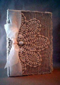 an old book with lace and pearls on it is sitting on a brown tablecloth