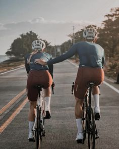 two bicyclists are riding down the road in front of each other with their arms around each other