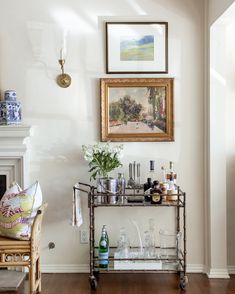 a bar cart with bottles and glasses on it in front of a painting hanging on the wall