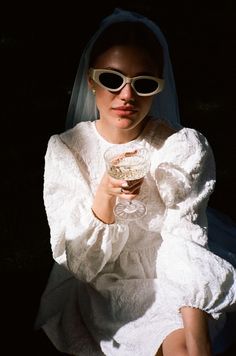 a woman in white dress and sunglasses holding a glass with food on top of it