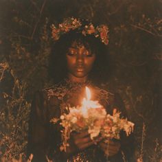 a young woman holding a lit candle in her hands and wearing a flower wreath around her head