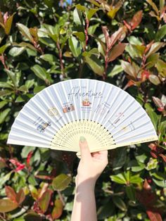 a person holding up a white fan in front of some bushes